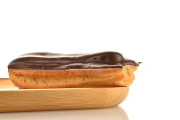 One delicious chocolate eclair on a bamboo tray, close-up, isolated on white.