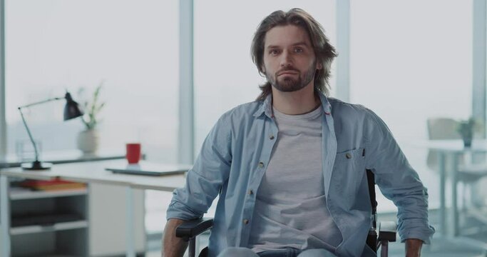 Portrait of handsome young caucasian worker male sitting in wheelchair smiling for camera. Corporate business people. Disabilitiesa. Car accident.