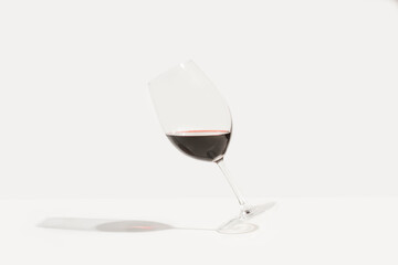 Copa de vino tinto cayendose sobre un fondo blanco liso y aislado y proyectando sombra. Vista de...