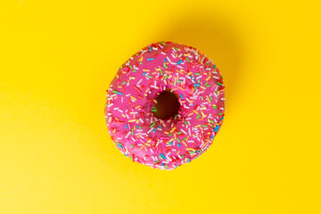 Round doughnut with pink icing, on a yellow background. Copy space. Top view. Flat lay