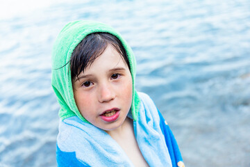 The boy  of nine years old in the towel is cold after a long swim in the sea. Child spending summer...