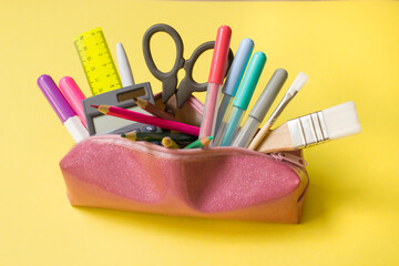 school pencil case with stationery, scissors, ruler, felt-tip pens, brushes, pencils on yellow background