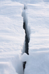 Vertical outdoor dramatic photo of a huge danger crack in the ice of glacier on a frozen lake at winter daytime
