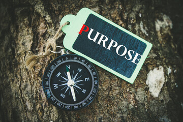 PURPOSE text written on wooden tag with magnetic compass  on old wooden background. A concept.