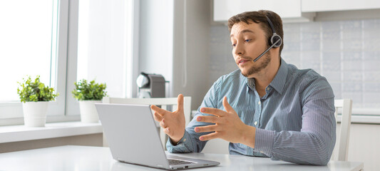 Man in front of laptop with headset during an online video call. Format 16:9.