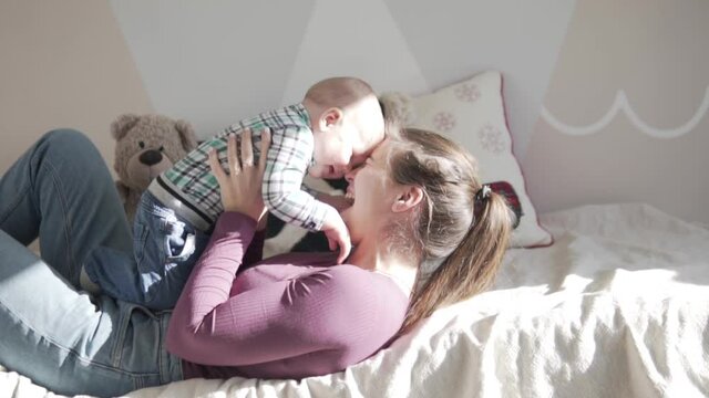 Young mother gently plays and kisses young son at home. Beautiful daylight