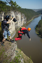 Basejumper jumps with a parachute from a cliff against the background of the river, the second athlete assists holds in his hand the string with the pilot chute pulling the canopy out of the knapsack.