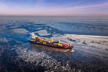 Cargo ship driving through frozen sea with colorful containers. Dark waters with ice blocks...