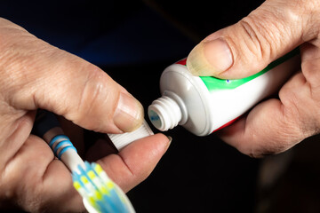 Female hands unscrew a tube of toothpaste and hold a toothbrush.