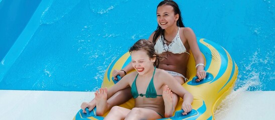 Two little girls on tube on water slide at aquapark. Summertime, vacation, entertainment, childhood...