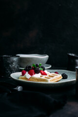 Belgian waffles with wild berries and cream cheese on a dark background