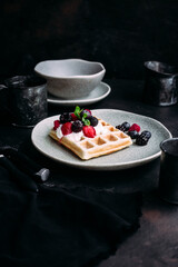 Belgian waffles with wild berries and cream cheese on a dark background