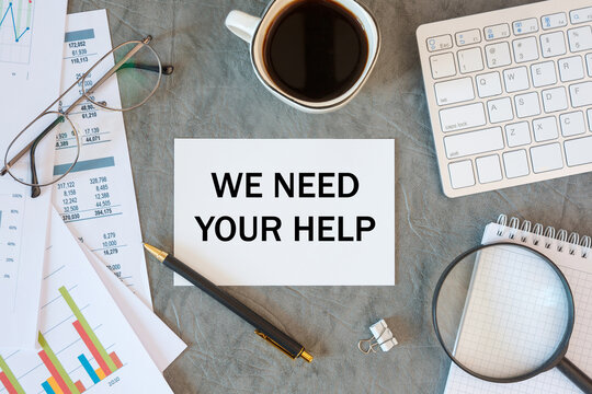 WE NEED YOUR HELPis written in a document on the office desk, coffee, diagram and smartfon