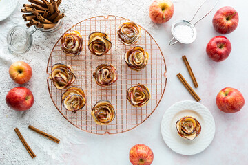 Top down view of apple rose pastries on a rose gold cooling rack with one pastry on a plate ready for eating.