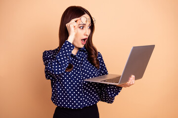 Naklejka premium Portrait of impressed pretty girl arm taking off eyewear open mouth look netbook isolated on beige color background