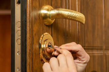 Male hands break open a brown front door with a lock pick close-up