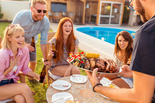 Host bringing plate of grilled meat to guests at backyard barbecue party