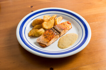 salmon recipe with potatoes and sauce on a plate and a wooden table