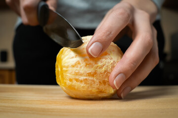 Female hands close up cutting a fresh peeled orange with a large knife in the kitchen