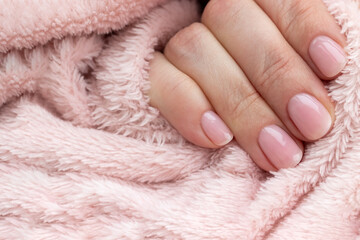 Female hands with beautiful manicure - pink nude nails on pale pink fluffy fabric, textile background, closeup with copy space