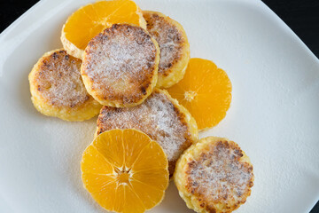 Cottage cheese pancakes with orange slices on a white plate sprinkled with powdered sugar. Beautiful, delicious breakfast