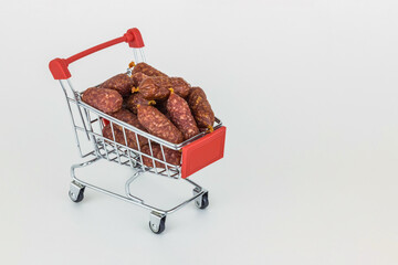 Metal shopping trolley with raw smoked sausage isolated on white with copy space. Meat food shopping concept.