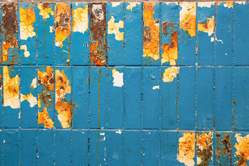 Colorful old industrial background.  Dirty blue cracked paint with chunks of flaking, and underneath, white tiles with orange rusty streaks and acid stains. 