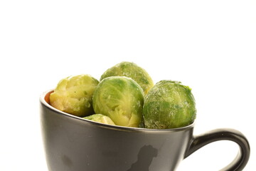 Several frozen organic Brussels sprouts in a ceramic bowl, close-up, isolated on white.