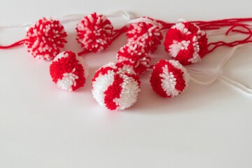 Close up red and white pompoms as martenitsa - bulgarian folklore tradition in March Baba Marta day. Shallow depth of focus, colorful yarn strains in couple of balls, light background.