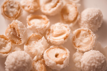 Cracked candy with almond and coconut flakes on white table closeup. Sweet tasty pastry. Top view.