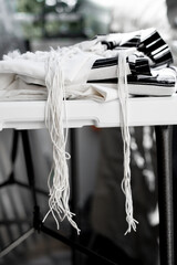 Black and white tallit lies on the table. White tassels (called tzitzit) hang down (260)