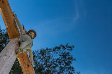 Fototapeta premium A figure of Jesus on a wooden roadside cross against a blue sky. Middle of the day, perfect lighting conditions.