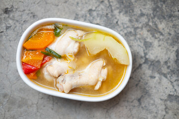 Boiled green soup winter melon with chicken drumsticks and carrot in a white ceramic bowl.