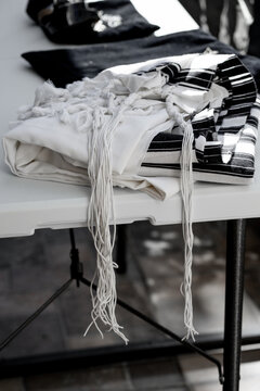 Black and white tallit lies on the table. White tassels (called tzitzit) hang down (261)