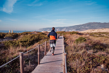 Fototapeta na wymiar Sports lifestyle. Man running on wooden pedestrian walkway through Sintra-Cascais natural park.