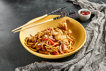 Hoisin chicken udon noodles. Yellow plate with wooden chopstick on dark slate table. Asian,...