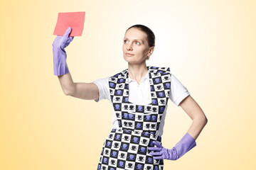 A beautiful young woman in the uniform of a maid holds a rag for washing windows. Isolated on a yellow background. Washes glass.