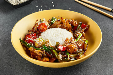 Sweet and Sour Chicken and Vegetables with Rice. Stir Fry Chicken with Vegetables and Sesame. Yellow plate with wooden chopstick on dark slate table. Chinese, asian, authentic food concept
