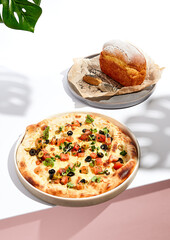Olives and Tomato Focaccia and Cornbread on white table. White table and monstera palm leaves in sunlight with hard shadow. Summer day food concept.
