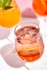 Cocktail garnished in wine glass with lemon slice and ice cube. Sunlight with hard shadow. Closeup view. Fresh, summer drink concept