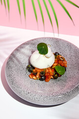 Burrata Cheese with Tomatoes and Olives. Restaurant appetizer plate on white table with pink wall. Day sunlight with hard shadow of fern palm leaves.