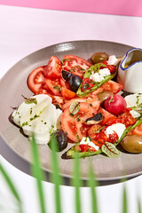 Tomato, olives and mozzarella salad . Restaurant appetizer plate on white table with pink wall. Day sunlight with hard shadow of fern palm leaves. Summer or spring restaurant food concept