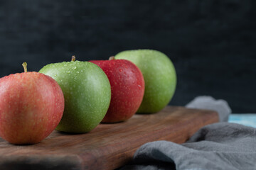 Red and green apples in a row on a wooden board