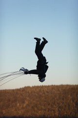 Black silhouette of a basejumper during a jump with an opened parachute, performing a front flip through the canopy, close-up.