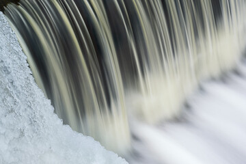 Winter landscape of the Battle Creek River cascade captured with motion blur and framed by icicles, Michigan, USA