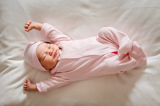 Cute little girl of 5 days in a pink jumpsuit lie on plaid and stretches in a dream in full height