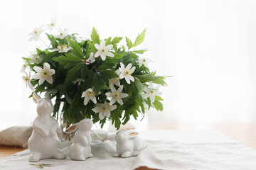 Happy Easter! Cute white bunnies and spring flowers on linen cloth napkin on rustic table in light