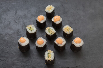 mini rolls are lined with Christmas trees on a black stone platter. Rice, cucumber, sesame, avocado, nori.