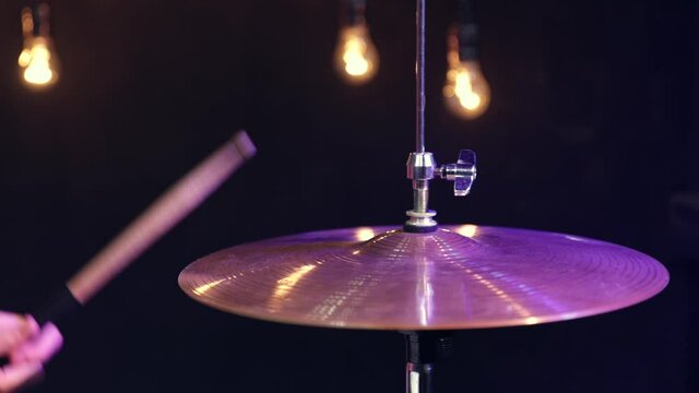 A man plays with sticks on a small hi-hat in a dark room with a beautiful light.