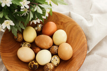 Happy Easter! Modern easter eggs in wooden bowl on rustic linen cloth with spring flowers. Aesthetic